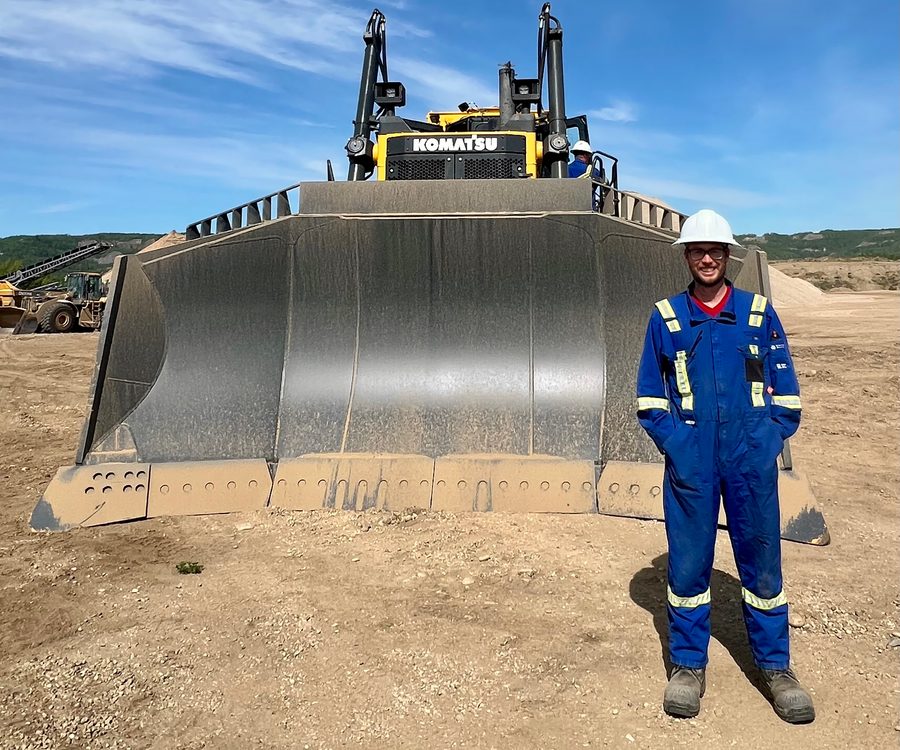 Jean-Pascal Remon in blue coveralls and a white hard hat, standing in front of the blade of a Komatsu dozer on a mine site.